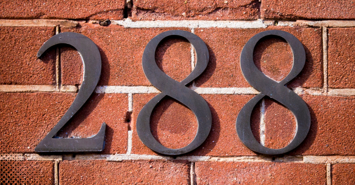 Close-up of black house numbers mounted on a red brick wall.